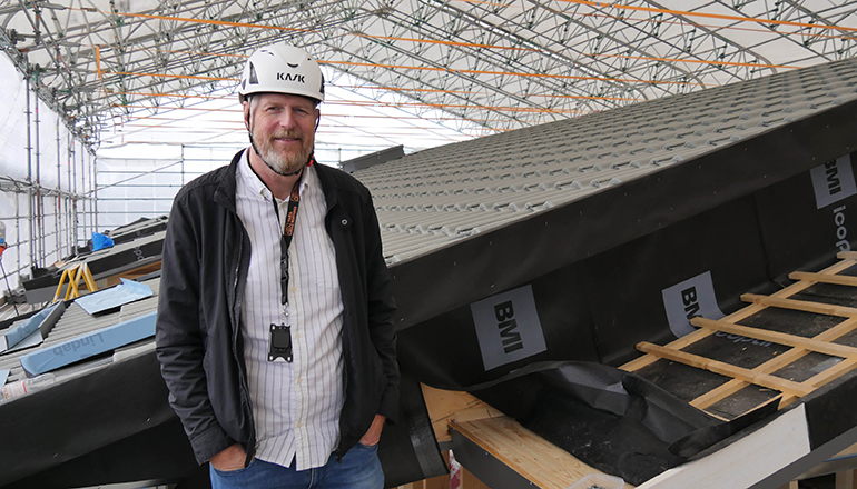 Man i bygghjälm står på ett tak på en byggarbetsplats.