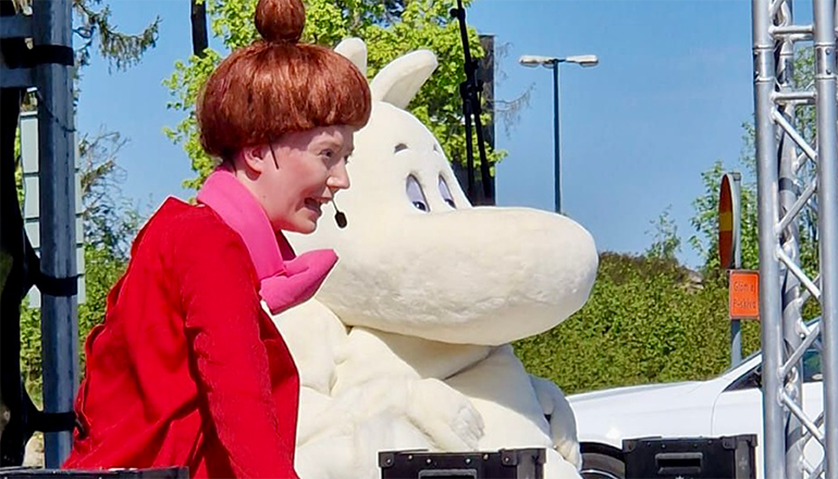 En kvinna med rött hår i knut och vitt mumintroll jämte.